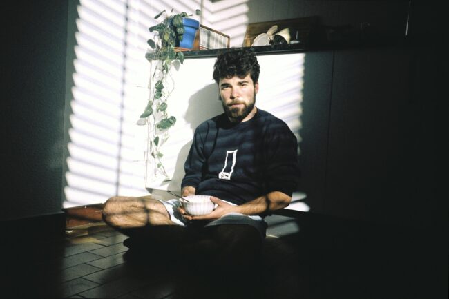 Jon Ander Urresti - Retrato plano medio. Sentado en el suelo de la cocina de un apartamento. Un recipiente en las manos.