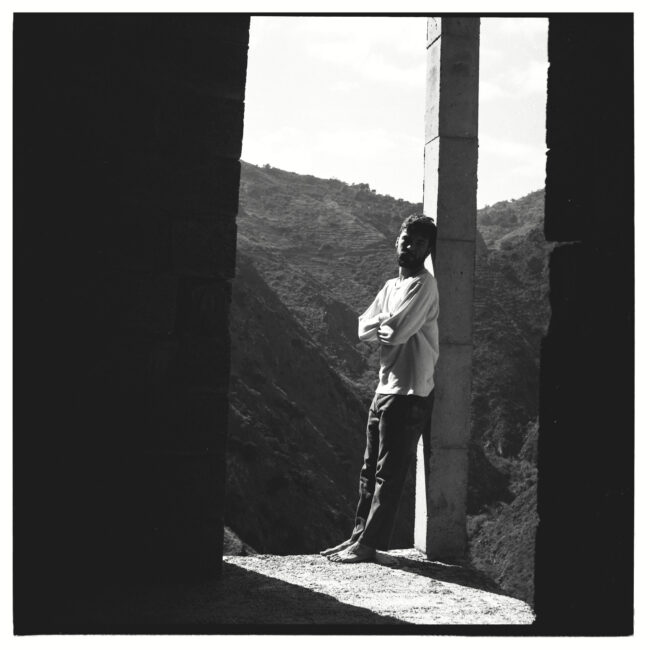 Jon Ander Urresti - Retrato de cuerpo entero. Blanco y negro. Apoyado a la columna de un balcón en un edificio en construcción. El monte, al fondo.