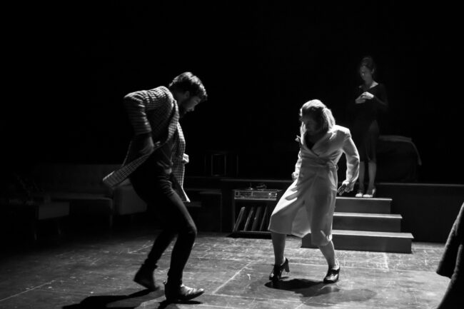 Jon Ander Urresti - Faces - Imagen de la obra de teatro. Blanco y negro. Dos personajes en escena, bailan en el centro del escenario. El personaje femenino, protagonizado por María Urcelay viste de blanco. El personaje de Jon Ander lleva una a mericana a cuadros. Estilo años 60.