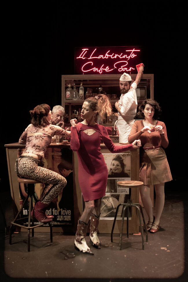 Jon Ander Urresti - La Sed del Minotauro - Imagen de la obra de teatro, dos actores y tres actrices ocupan la escena en torno a la barra de un bar con un letrero luminoso que lee 